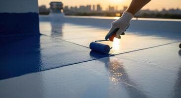 gloved-hand-applying-blue-waterproof-coating-with-a-paint-roller-on-a-rooftop-at-sunset-photo
